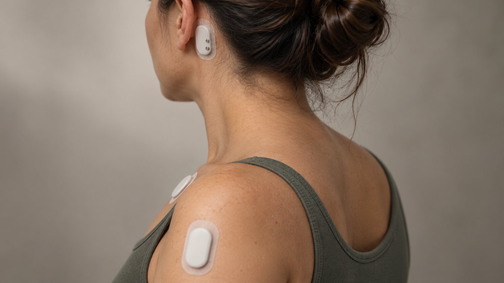 Concept render: a volunteer seen from behind wearing three small white sensor patches — behind the left ear, on the shoulder and on the upper arm